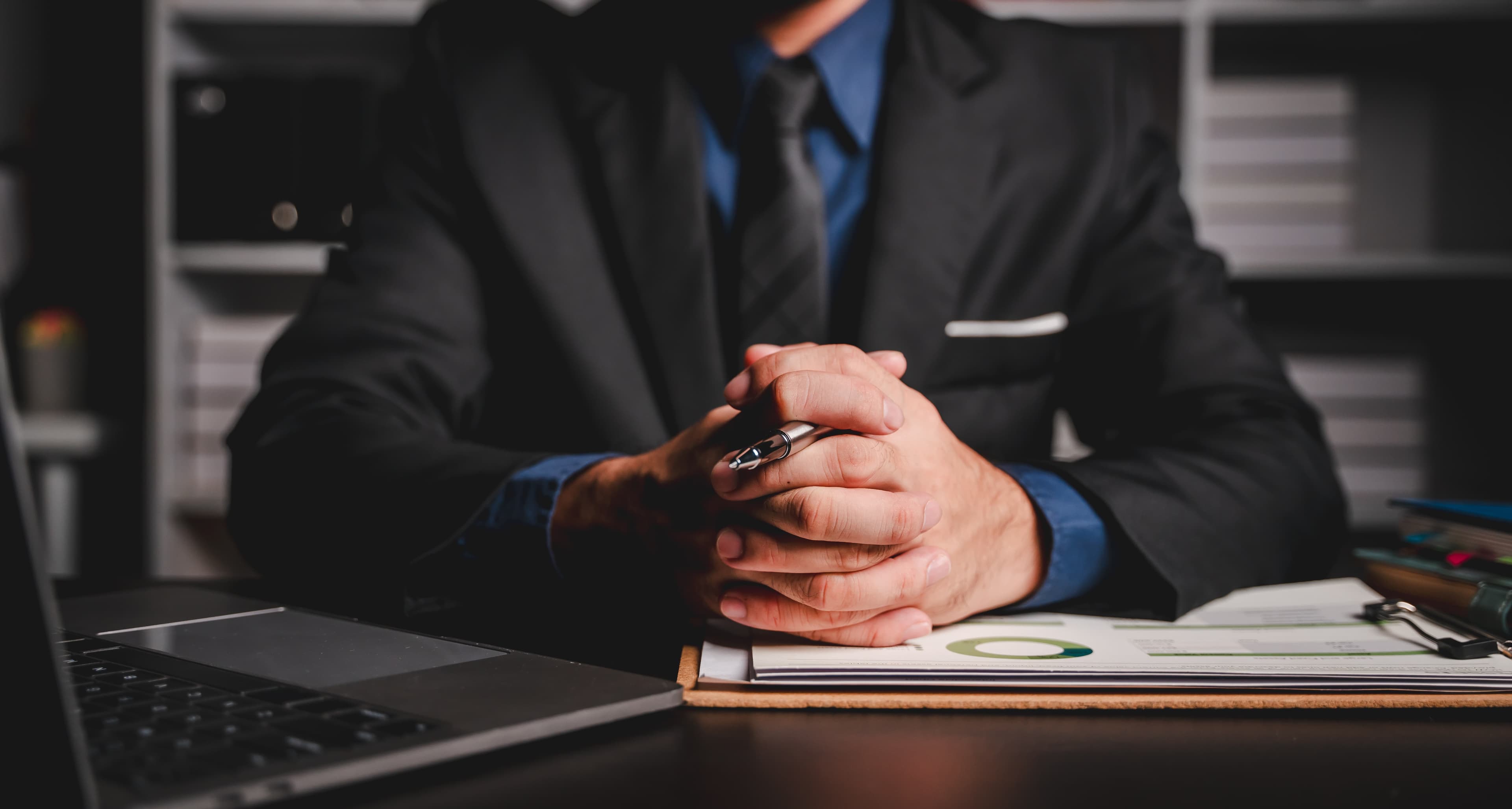 man with pen in his hands sitting formally at the desk